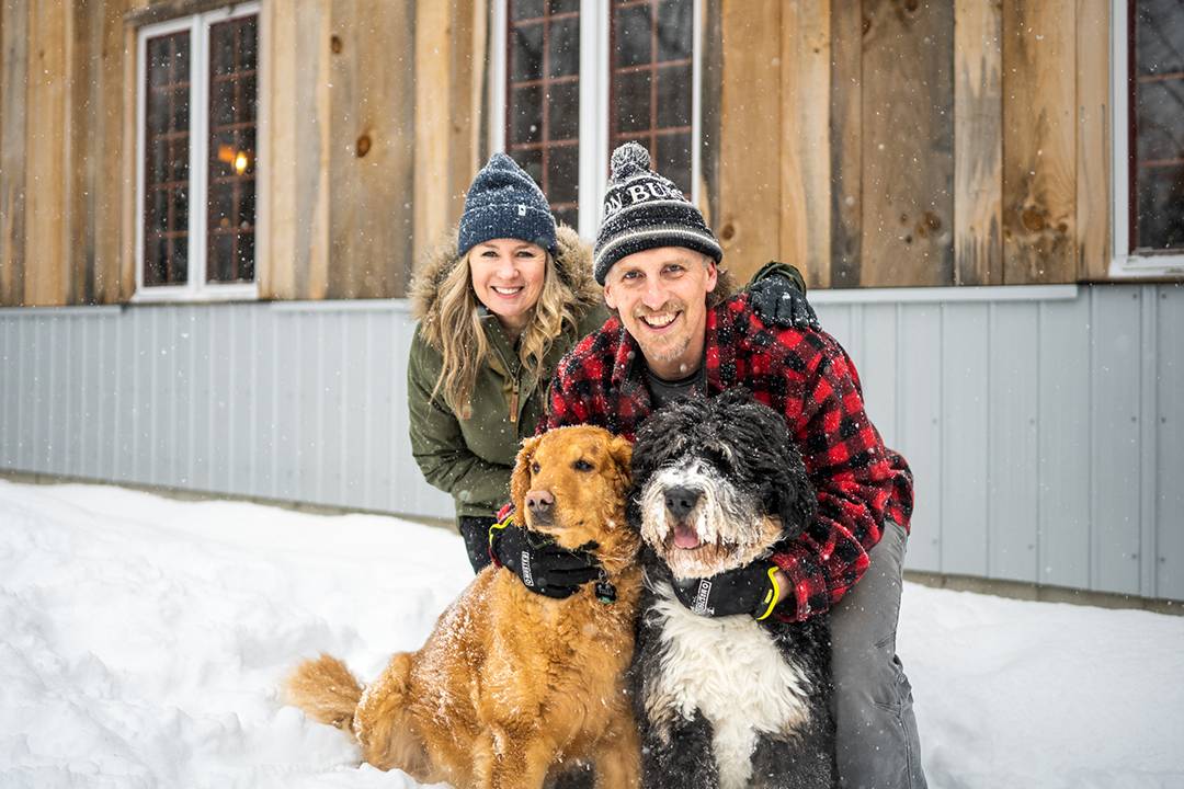 Elysa Walk and Dan Fuller pose for a photo with loyal companions Tilly (left, golden retriever) and Roscoe (right, bernadoodle) in front of Clean Maple’s Sugarhouse